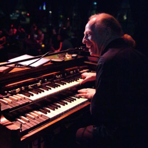 Musician playing keyboard on stage, smiling.